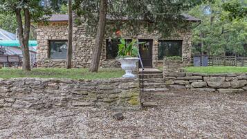A stone building with a stone wall in front, a large planter with plants, and a wooden fence in the background.