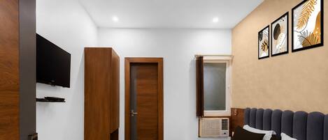 A hotel room with a bed, a television, a wardrobe, a door, and a window.