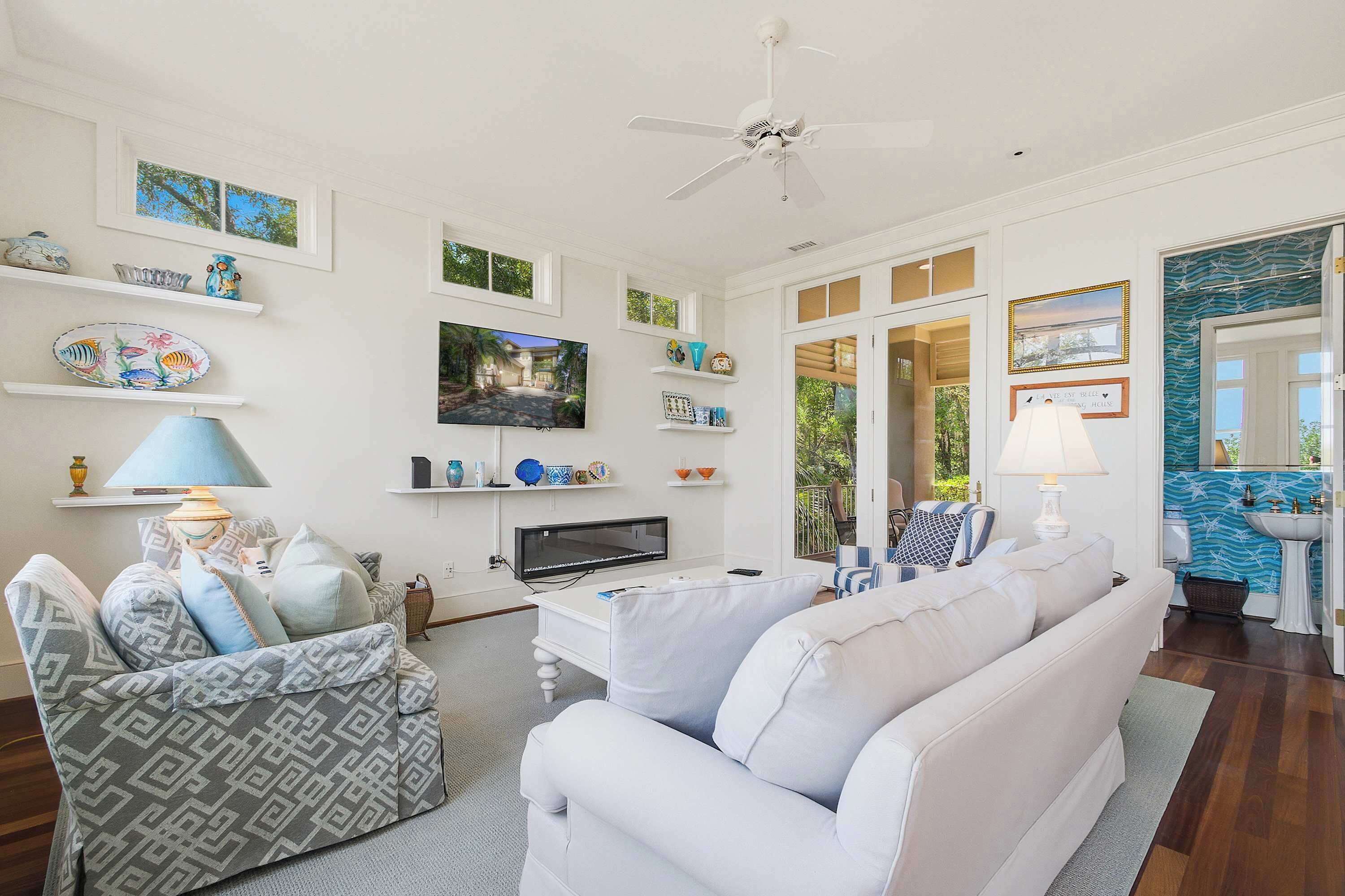 A living room with a white sofa, a television, and decorative items on shelves.