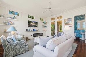 A living room with a white sofa, a television, and decorative items on shelves. - Elegant Lowcountry Retreat | Marsh Views, Decks & Elevator (Johns Island)