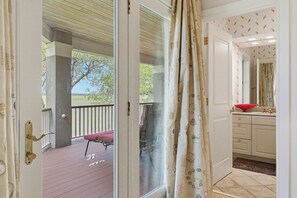 A room with a sliding glass door leading to an outdoor deck with a bench and a tree. - Elegant Lowcountry Retreat | Marsh Views, Decks & Elevator (Johns Island)