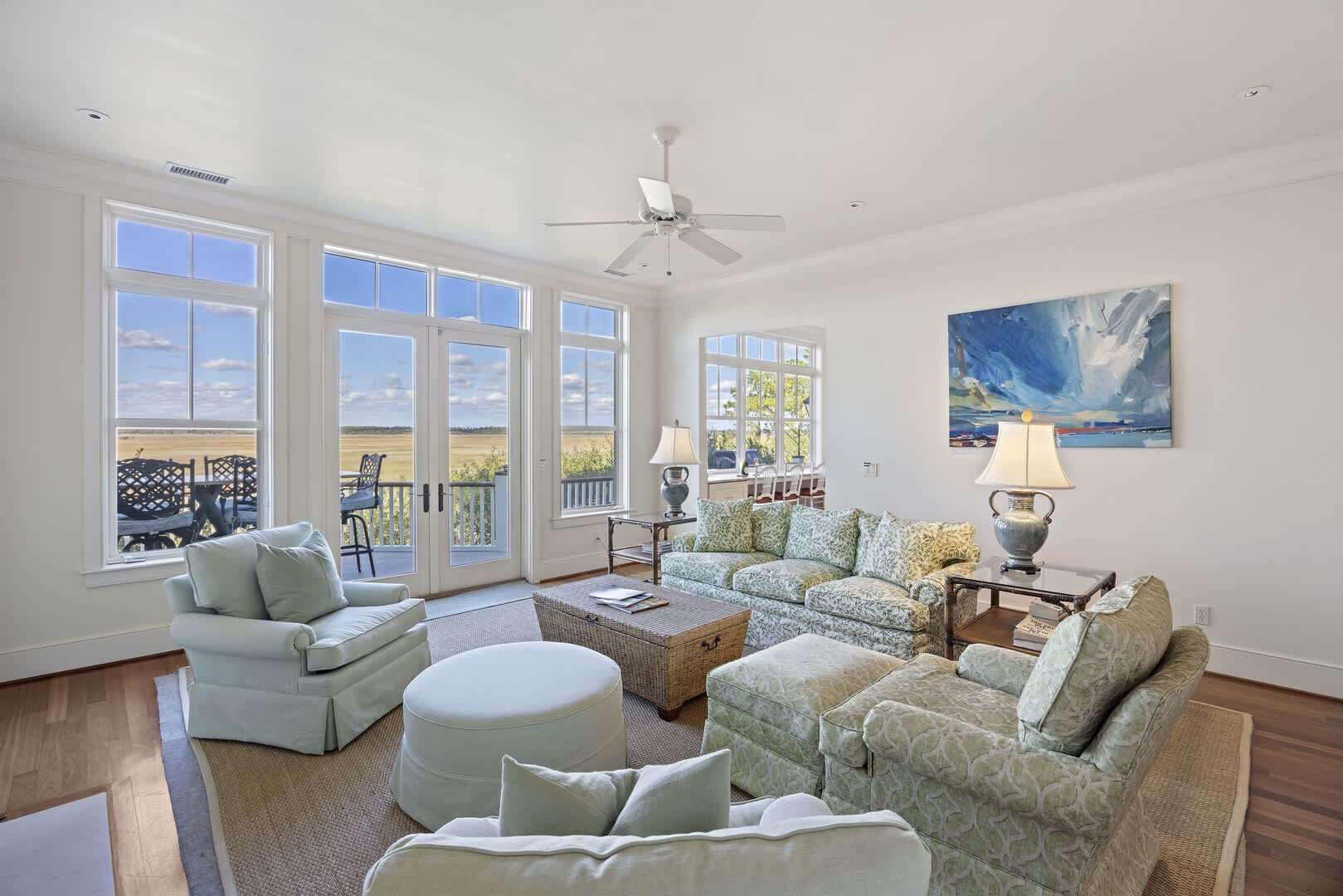 A spacious living room with a large window, a ceiling fan, and a painting on the wall.