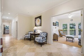 A spacious hallway with a dining area featuring two chairs and a table, a large floral painting on the wall, and a view of an outdoor balcony. - Elegant Lowcountry Retreat | Marsh Views, Decks & Elevator (Johns Island)