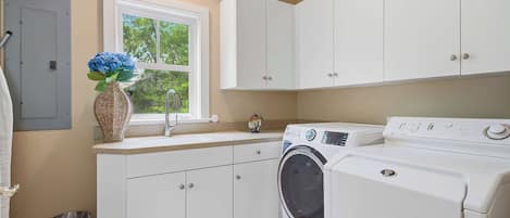 Une buanderie équipée d’un lave-linge, d’un évier et de placards.