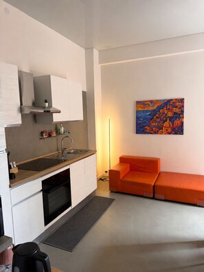 A modern kitchen with a built-in oven, a sink, and a stove. There is a small dining area with a sofa and a painting on the wall. - An elegant open-concept space in Salerno's harbor area, just a short walk from downtown. (Salerno)