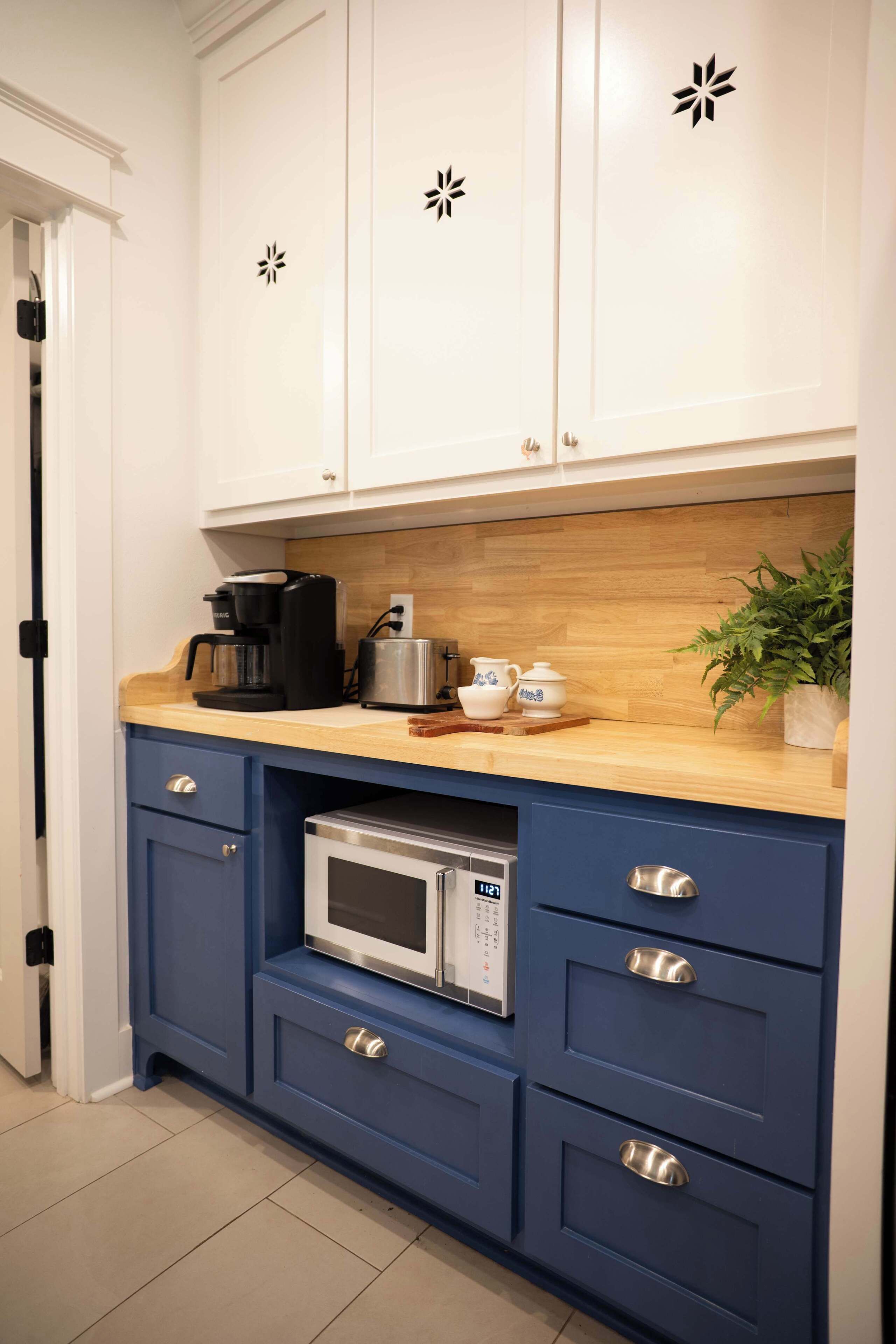 Een keuken met witte kasten, een houten aanrecht, een ingebouwde magnetron en een koffiezetapparaat.