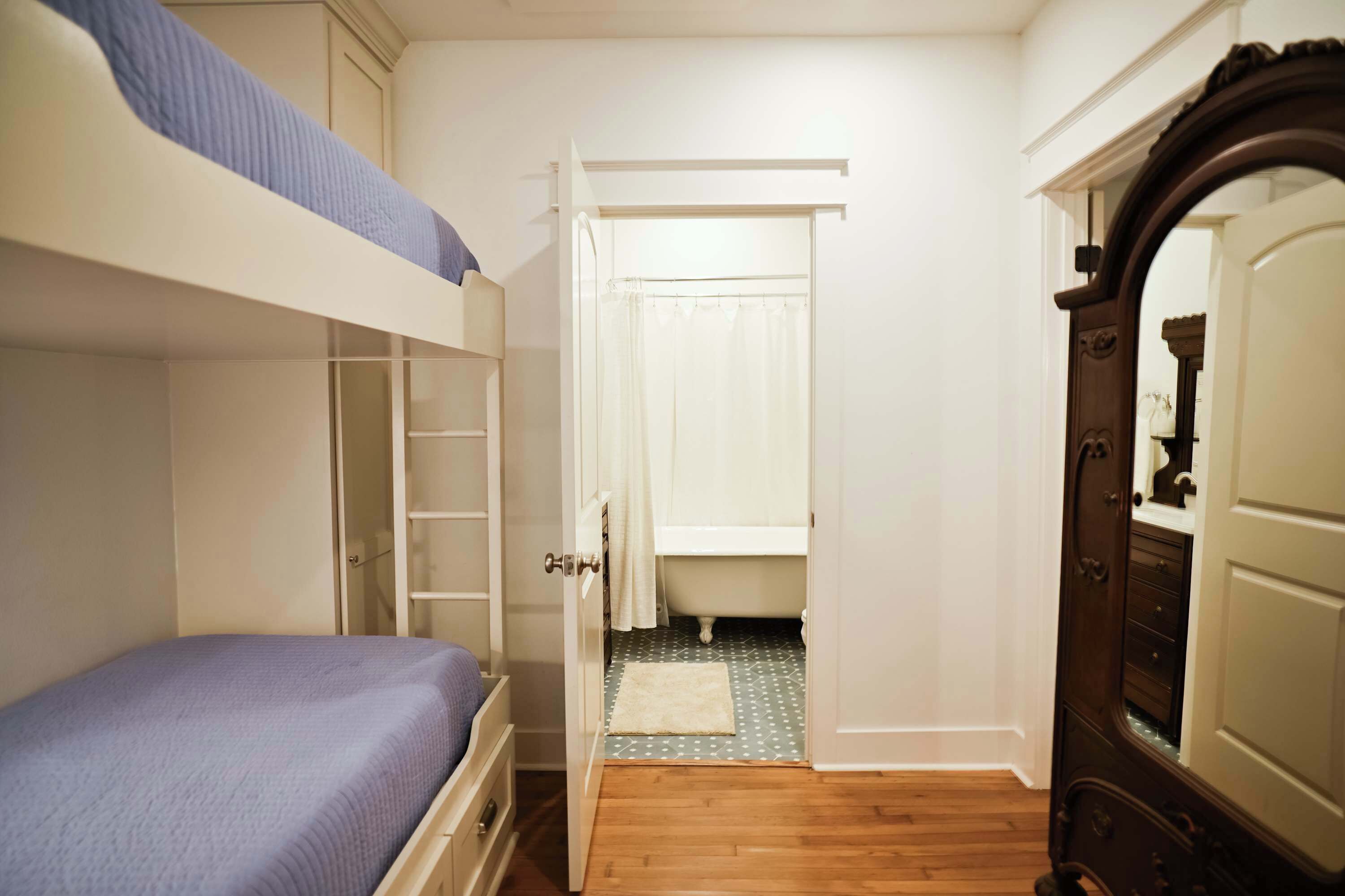 A bedroom with a bunk bed, a wardrobe, and a bathroom visible through an open door.