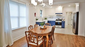 Une cuisine moderne avec un coin repas, comprenant une table et des chaises en bois, un lustre et une grande fenêtre avec des rideaux.