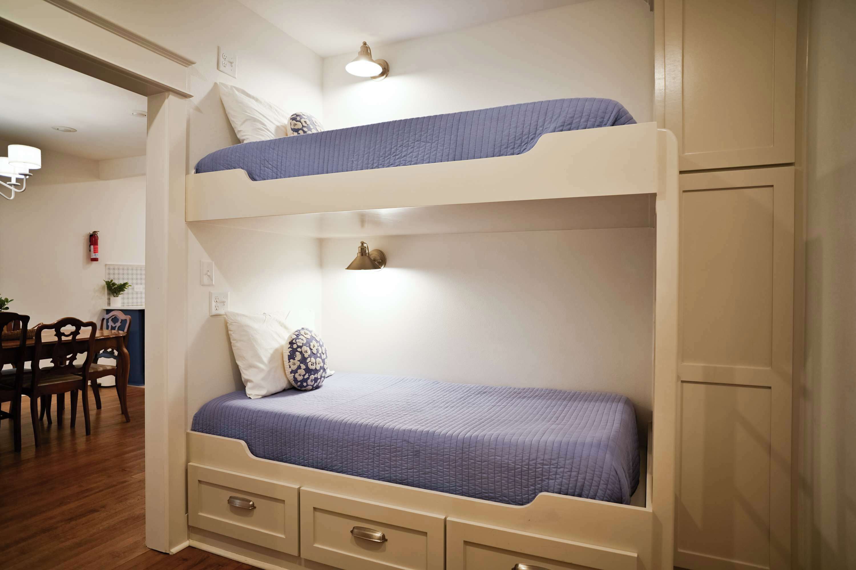 Una cama litera con escritorio y silla, una lámpara de pared y un extintor.
