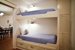 Un lit superposé avec un bureau et une chaise, une lampe fixée au mur et un extincteur.
