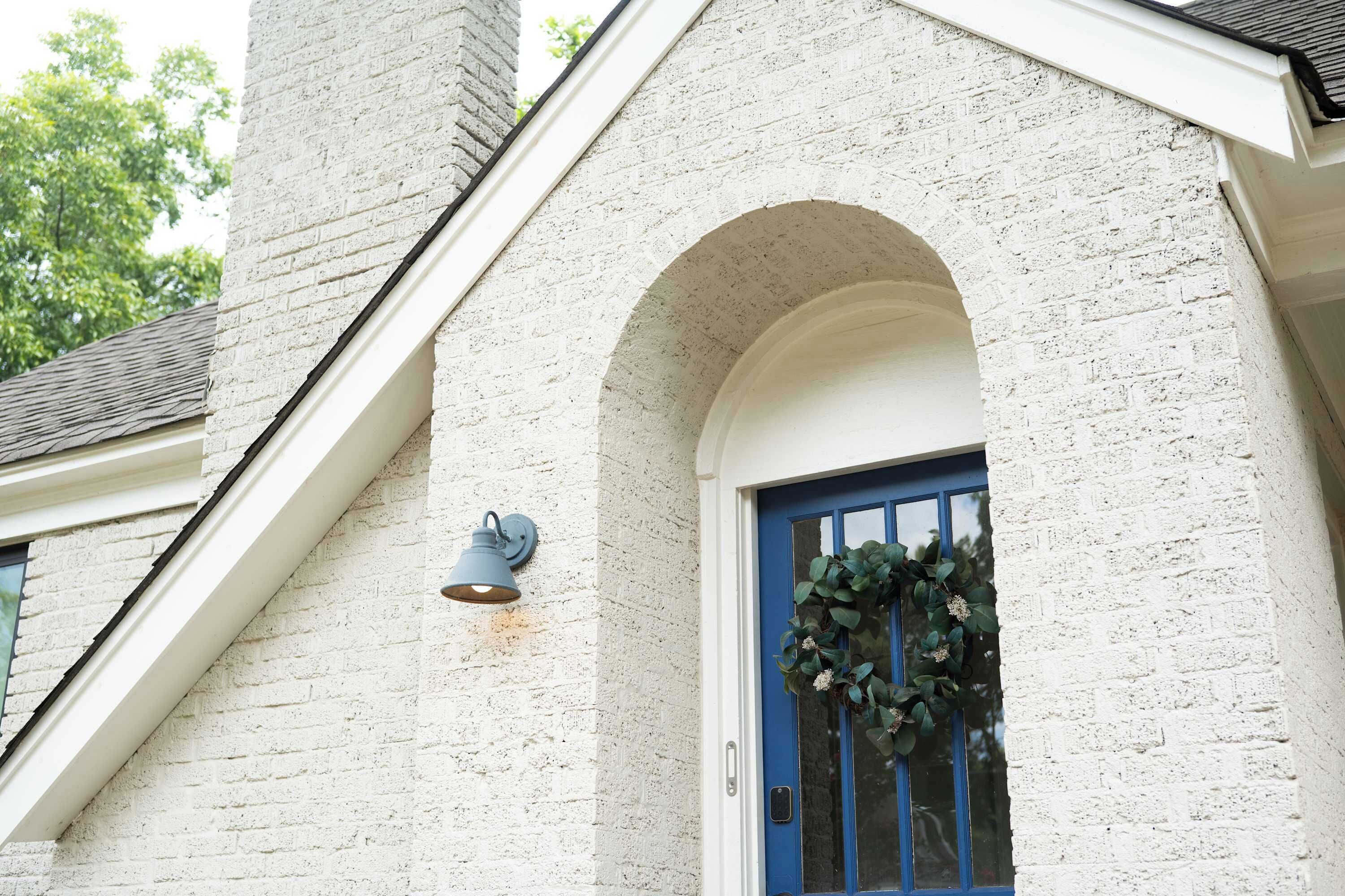 Een gebouw met een witte bakstenen gevel, een blauwe deur en een wandlamp.