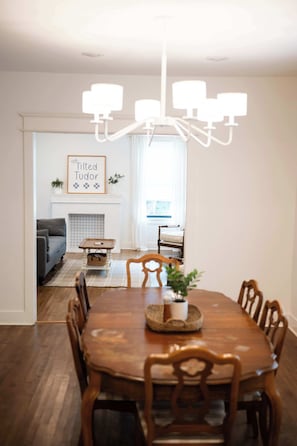 A dining area with a wooden table and chairs, a chandelier, a fireplace, and a framed sign on the wall.