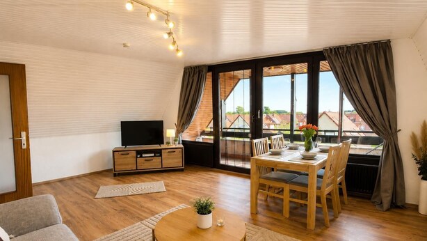 En moderne stue med et fladskærms-tv, træmøbler, et spiseområde med bord og stole samt store vinduer med gardiner.