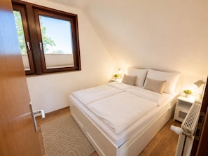 Ein Schlafzimmer mit Bett, Nachttischen, Heizkörper, Fenster und Tür.