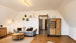 Et moderne loftværelse med skråvæg, en grå sofa, et træskab og et spisebord.