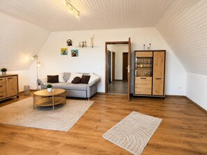 Ein modernes Schlafzimmer im Loft-Stil mit schrägem Dach, einem grauen Sofa, einem Holzschrank und einem Esstisch.