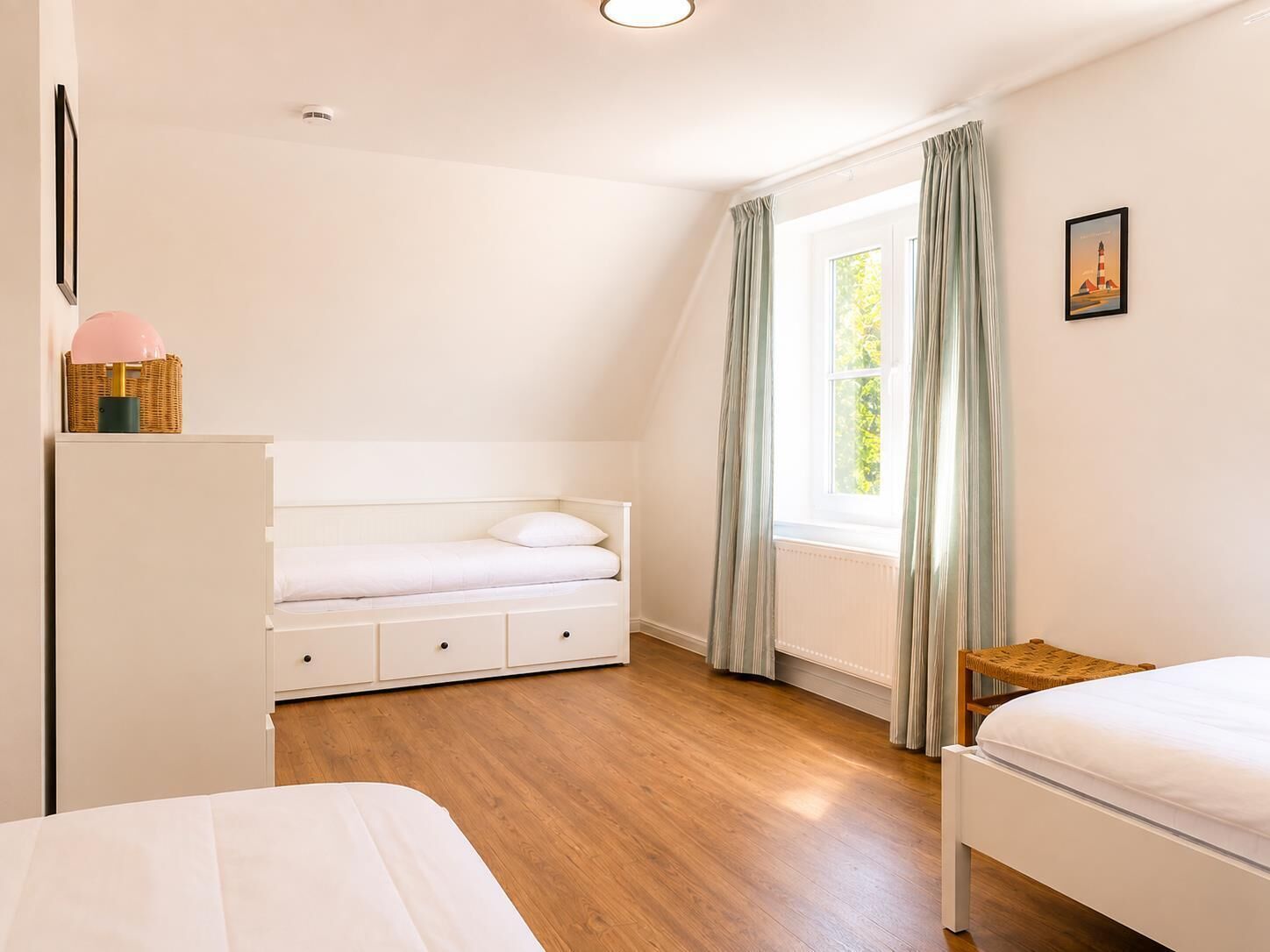 Ein Schlafzimmer mit einem Bett, einer Kommode, einem Fenster mit Vorhängen und einem Bild an der Wand.