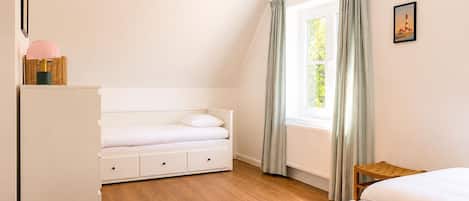 Ein Schlafzimmer mit einem Bett, einer Kommode, einem Fenster mit Vorhängen und einem Bild an der Wand.