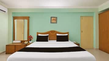 A hotel room with a bed, a bedside table, a mirror, a picture on the wall, and a door.
