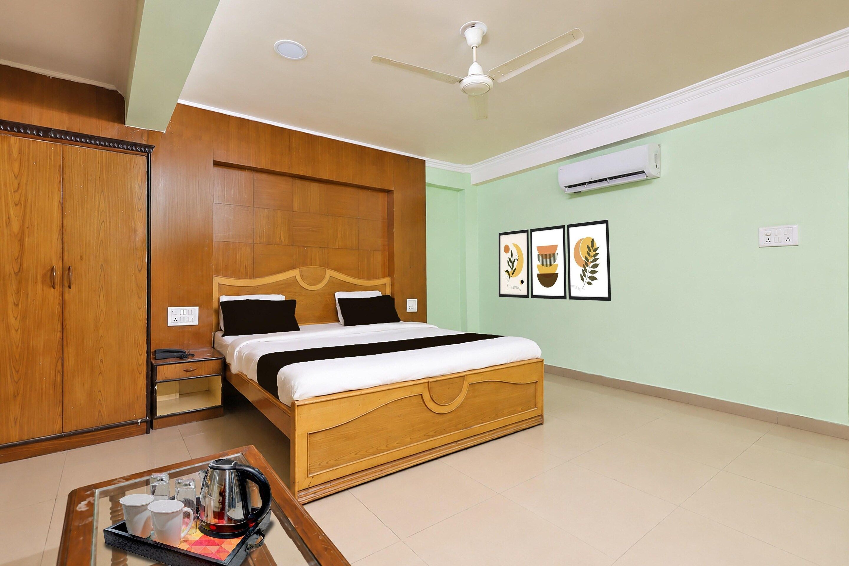Une chambre d’hôtel avec un lit en bois, une table de chevet, une table basse avec un plateau, un appareil de climatisation et un ventilateur de plafond.