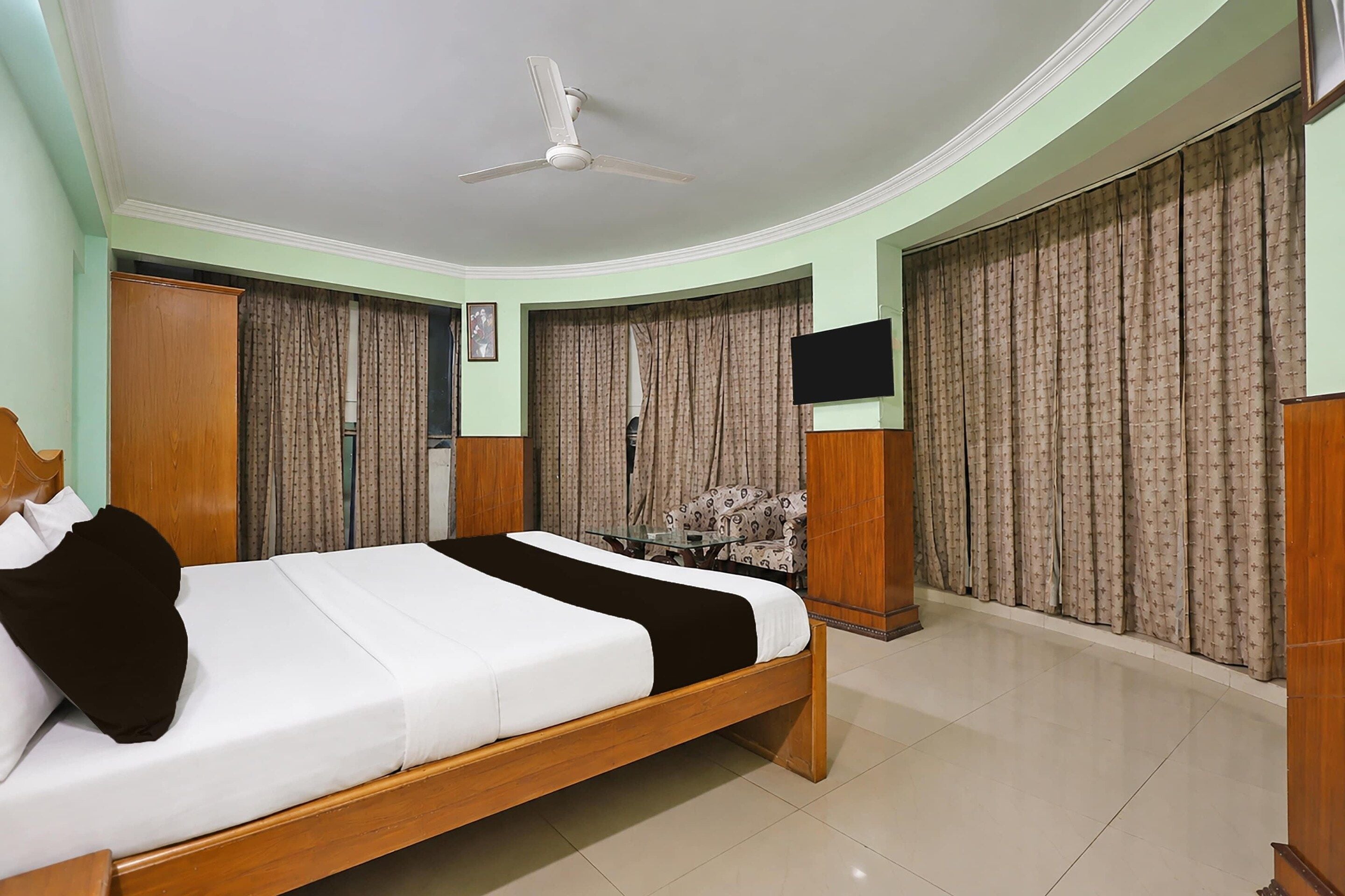 A bedroom with a bed, a ceiling fan, a TV, and curtains.