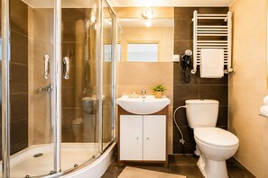 Un baño moderno con ducha envuelta en vidrio, un lavamanos blanco con espejo, un inodoro y un perchero para toallas.