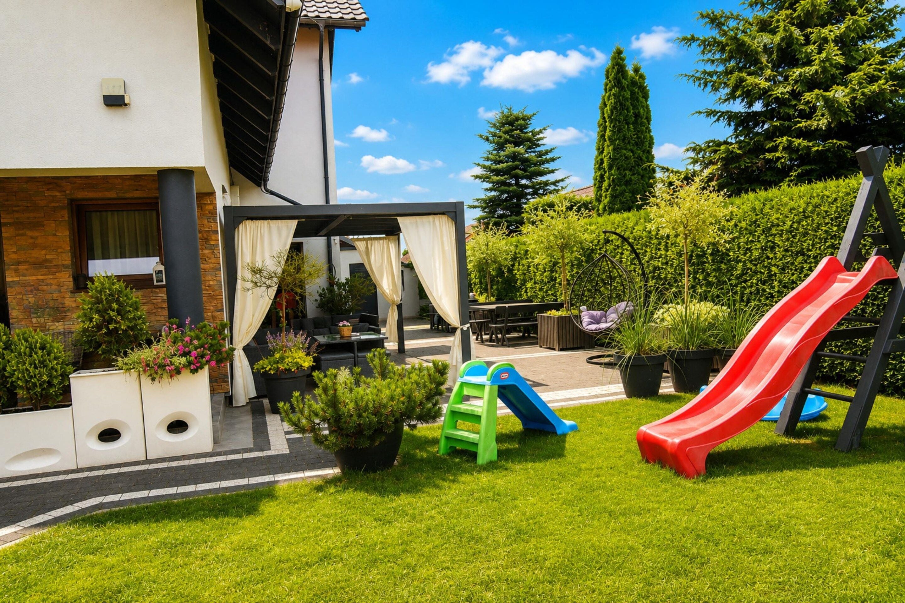 Een woongebied buiten met een terras, zitplaatsen, een speelstructuur en een tuin.
