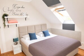 A bedroom with a sloped ceiling, a bed with two pillows, a bedside table with a lamp, and a wall-mounted shelf with a plant. - Studio for 2 People, Close to the sea (Kamien Pomorski)