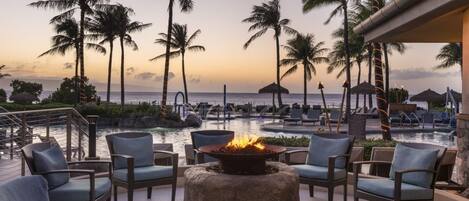 A resort pool area with lounge chairs and a fire feature, overlooking the ocean.