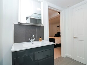 A modern bathroom with a white sink, dark cabinets, and a large mirror. - Shipwrights (Brixham)