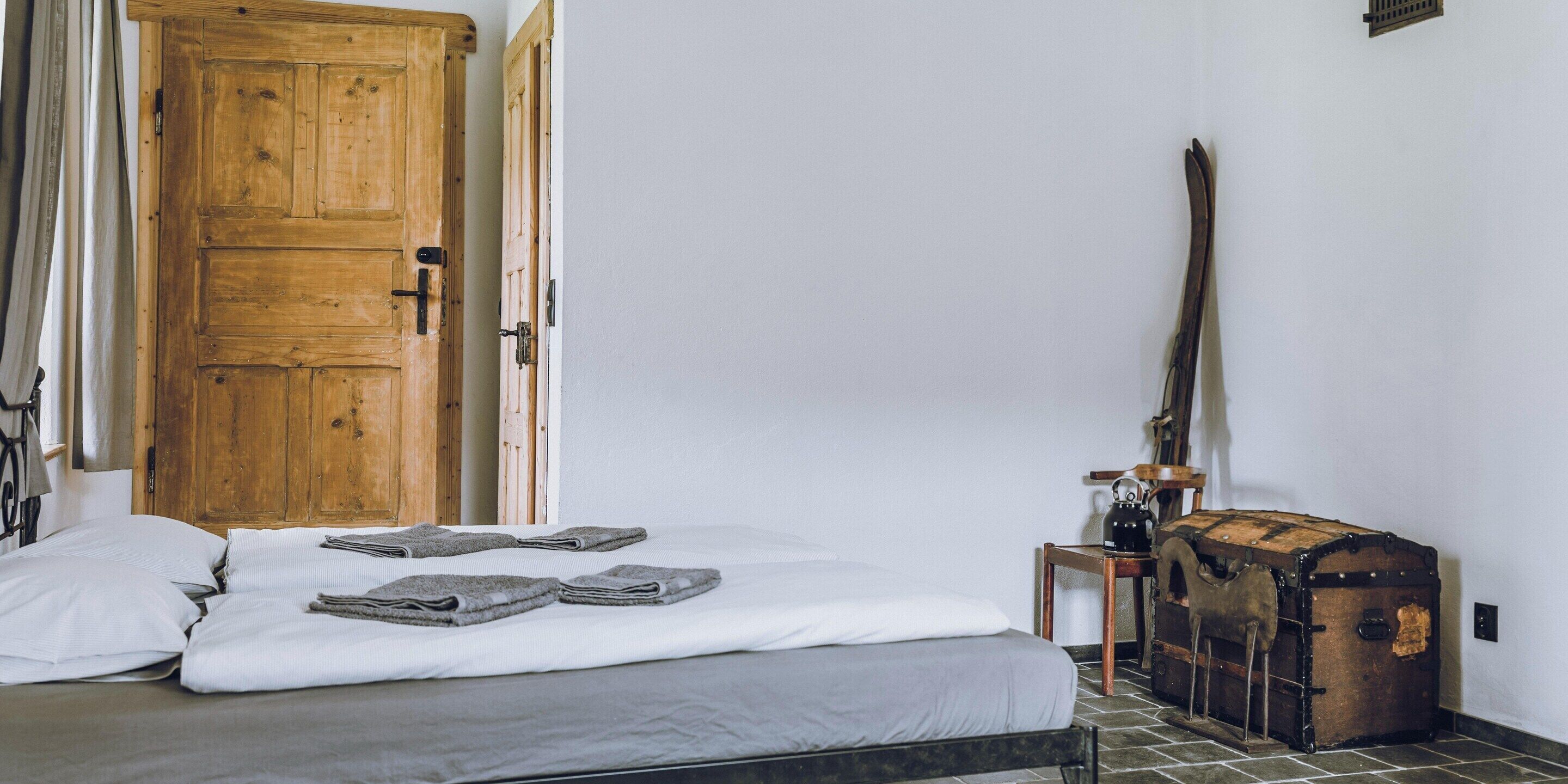 A room with a bed, a wooden door, a suitcase, and a lamp.