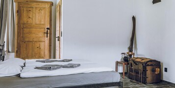 Una habitación con una cama, una puerta de madera, una maleta y una lámpara.