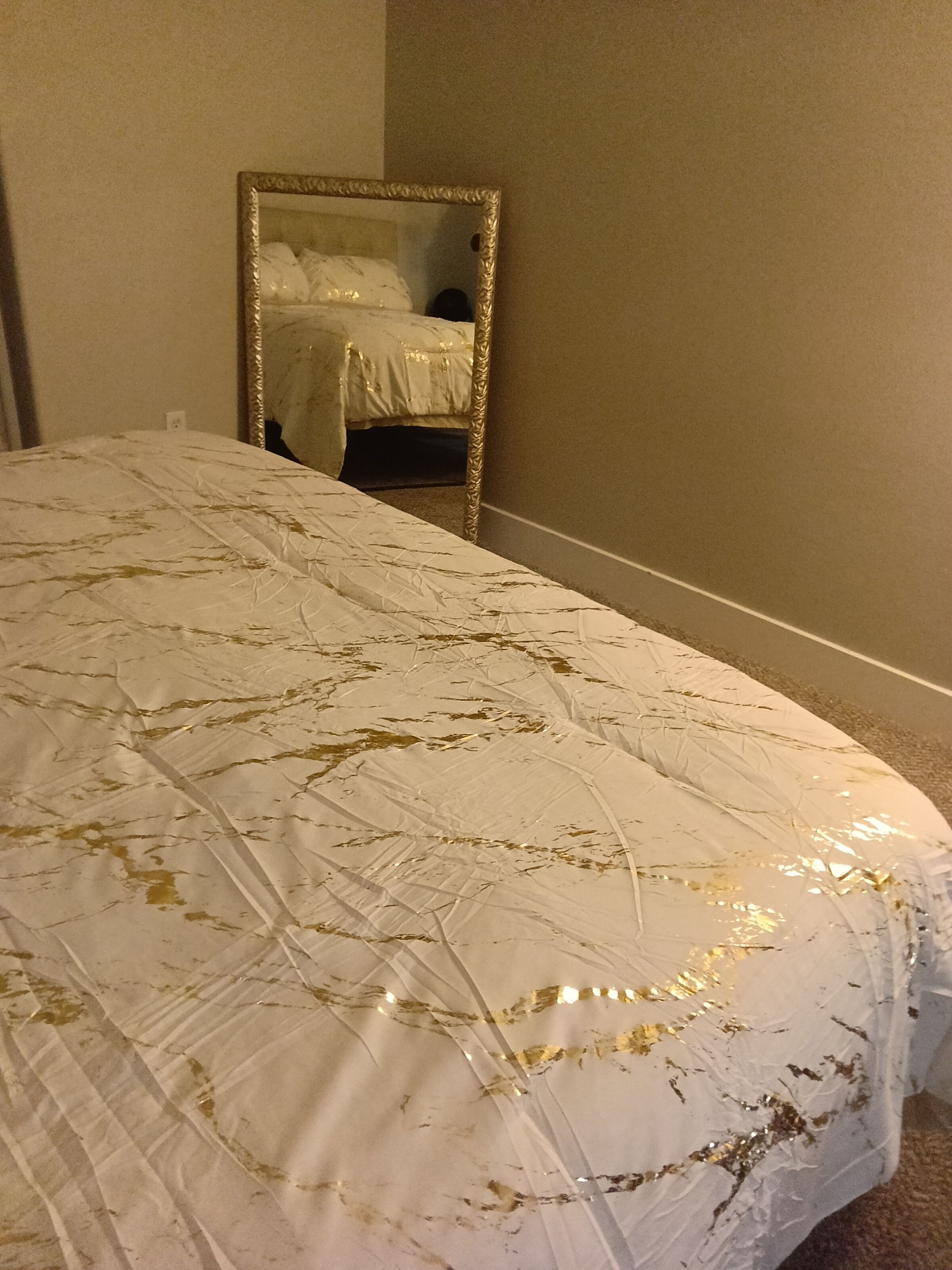 Ein Bett mit gemustertem Überwurf, ein Spiegel an der Wand und ein Teppichboden.