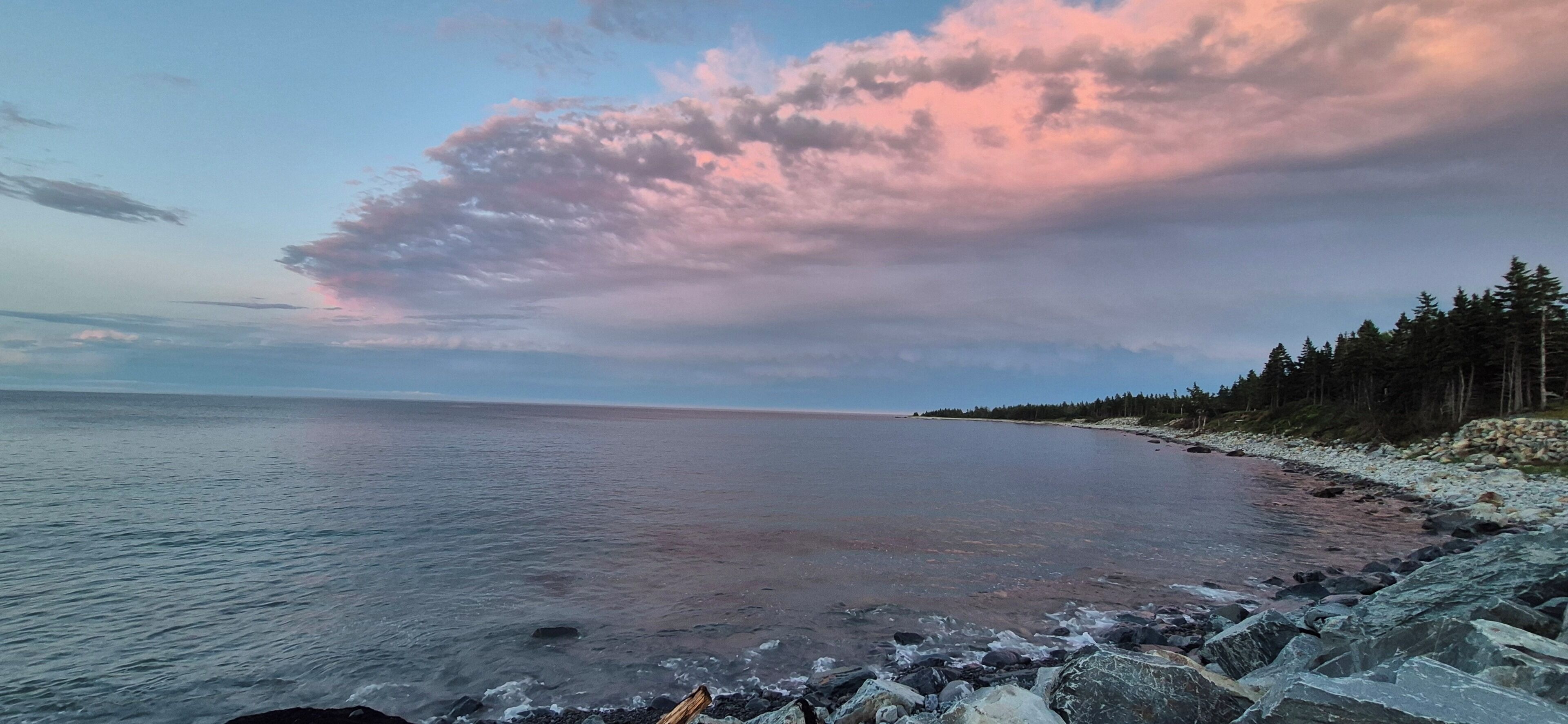 Un paysage côtier caractérisé par une rive rocheuse, une mer calme et une zone boisée à l’horizon.