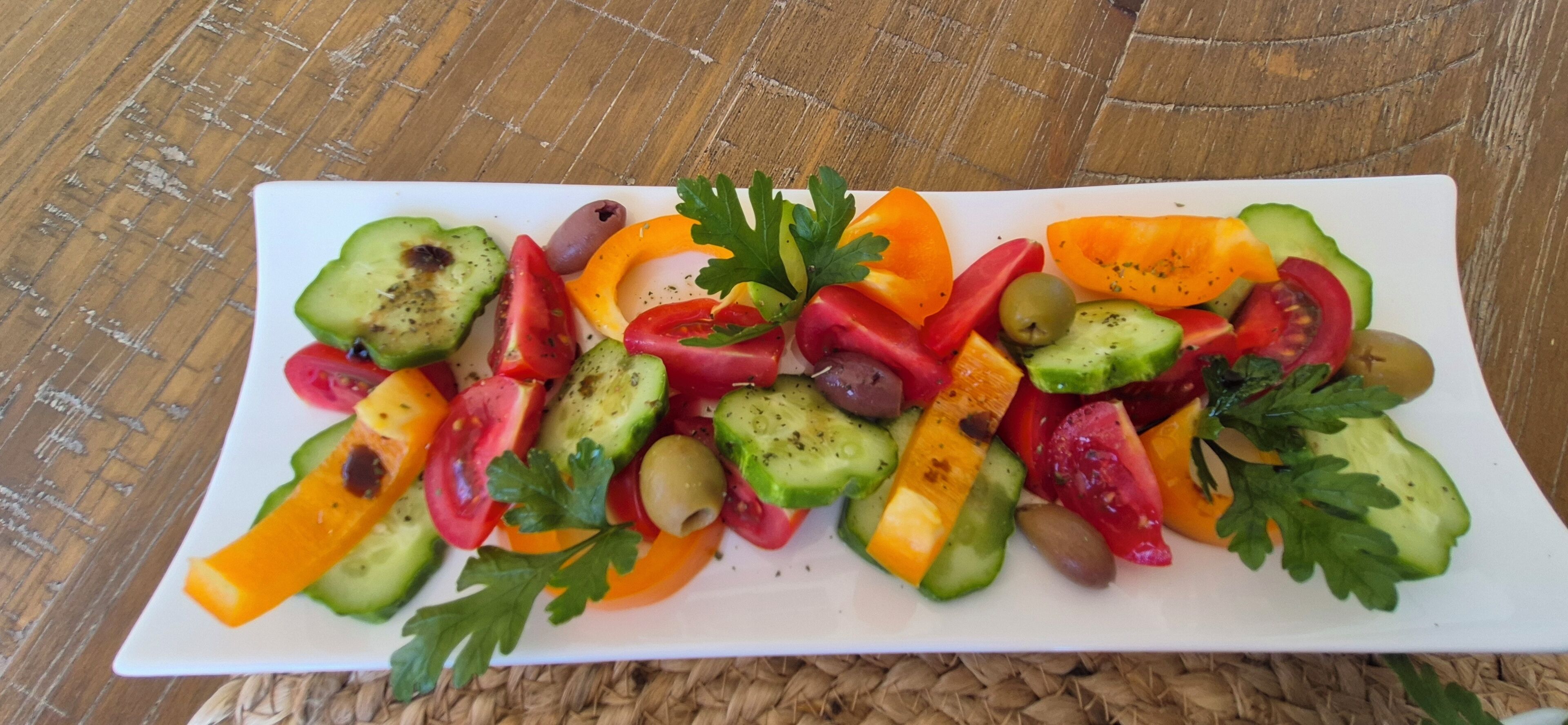 Plat rectangular blanc amb diverses verdures tallades i olives, guarnit amb julivert, sobre un suport de tela.