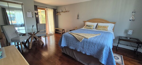 A hotel room with a bed, a chair, a small table, and a window with curtains.
