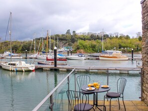A marina with boats docked, a table with chairs and breakfast items, and a stone building in the background. - Spanish Boathouse (Brixham)