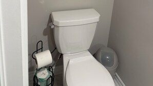 Un baño con inodoro, rollo de papel higiénico y un cubo de basura.