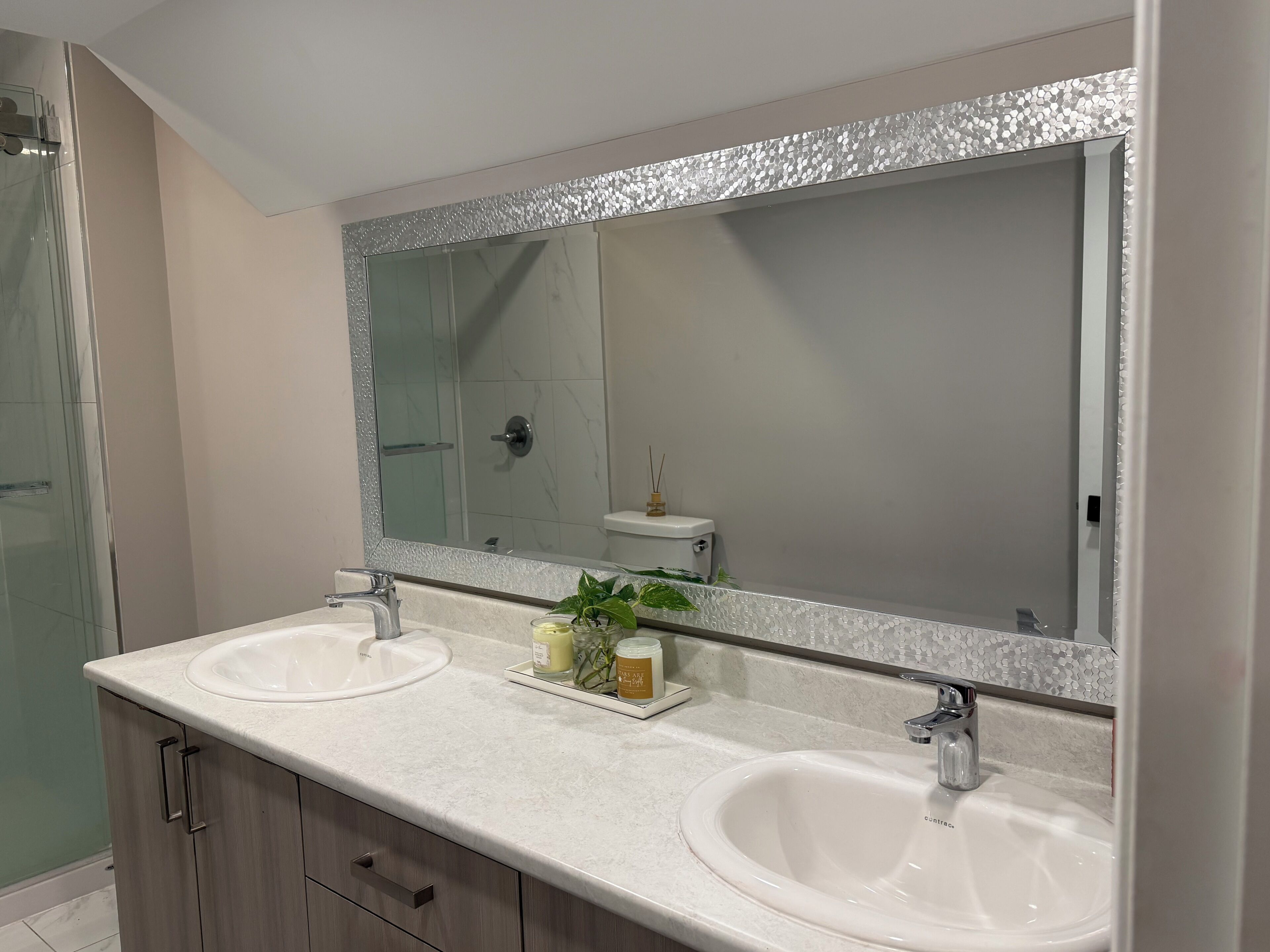 A bathroom with two sinks, a large mirror, and a shower.