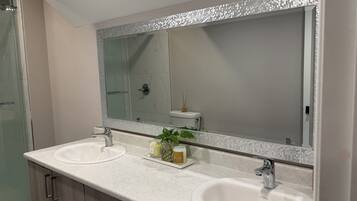 A bathroom with two sinks, a large mirror, and a shower.