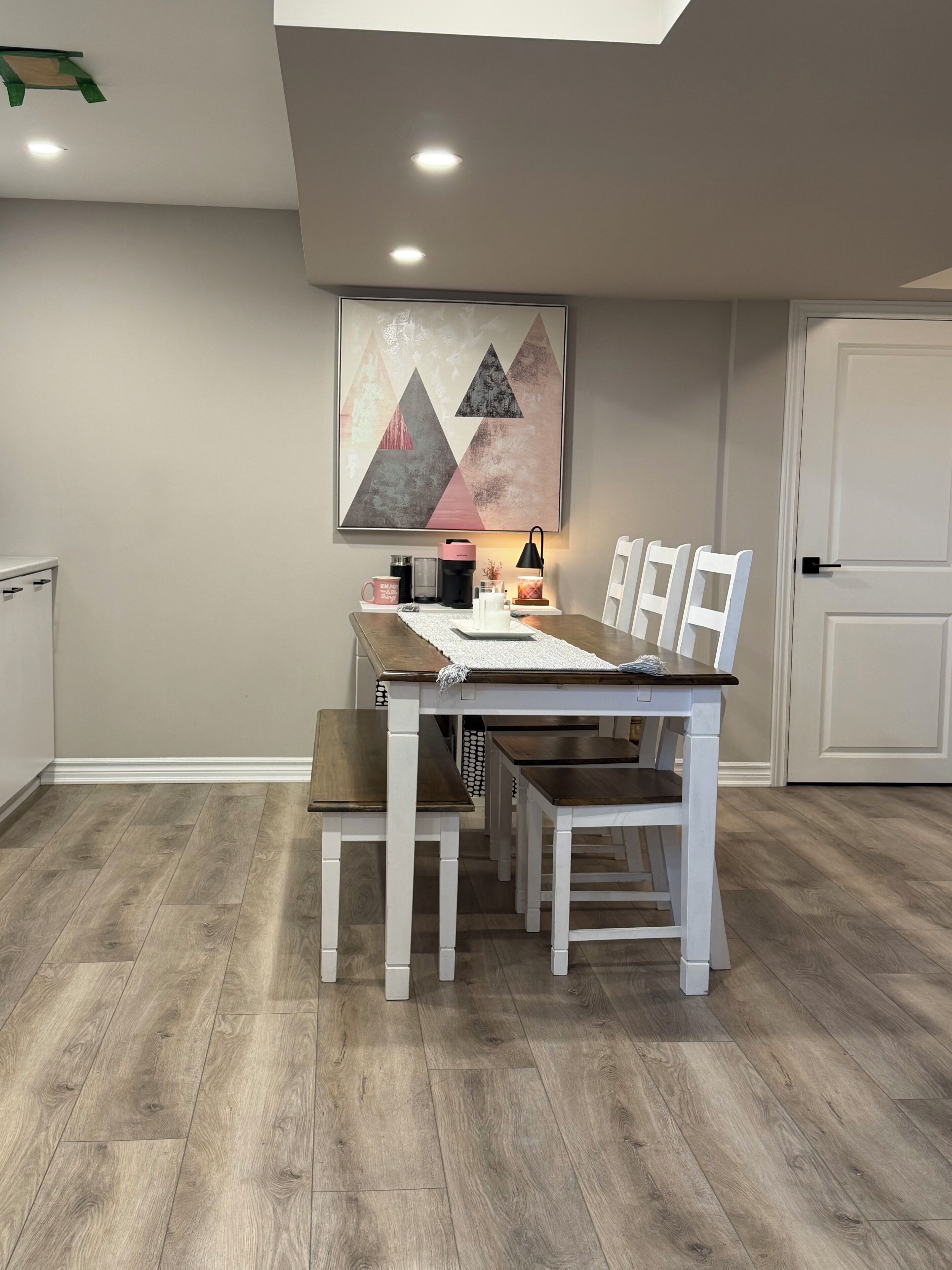A dining area with a table and chairs, a painting on the wall, and a door in the background.