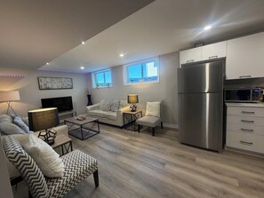 A modern living room with a sofa, armchair, coffee table, and a flat-screen TV.