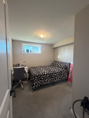 A bedroom with a bed, a desk, a chair, a window, and a red telephone booth.