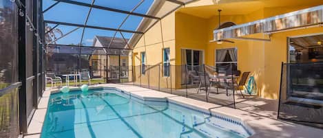 Una piscina interior con cerramiento de vidrio, rodeada de paredes amarillas y un área de patio con mobiliario exterior.