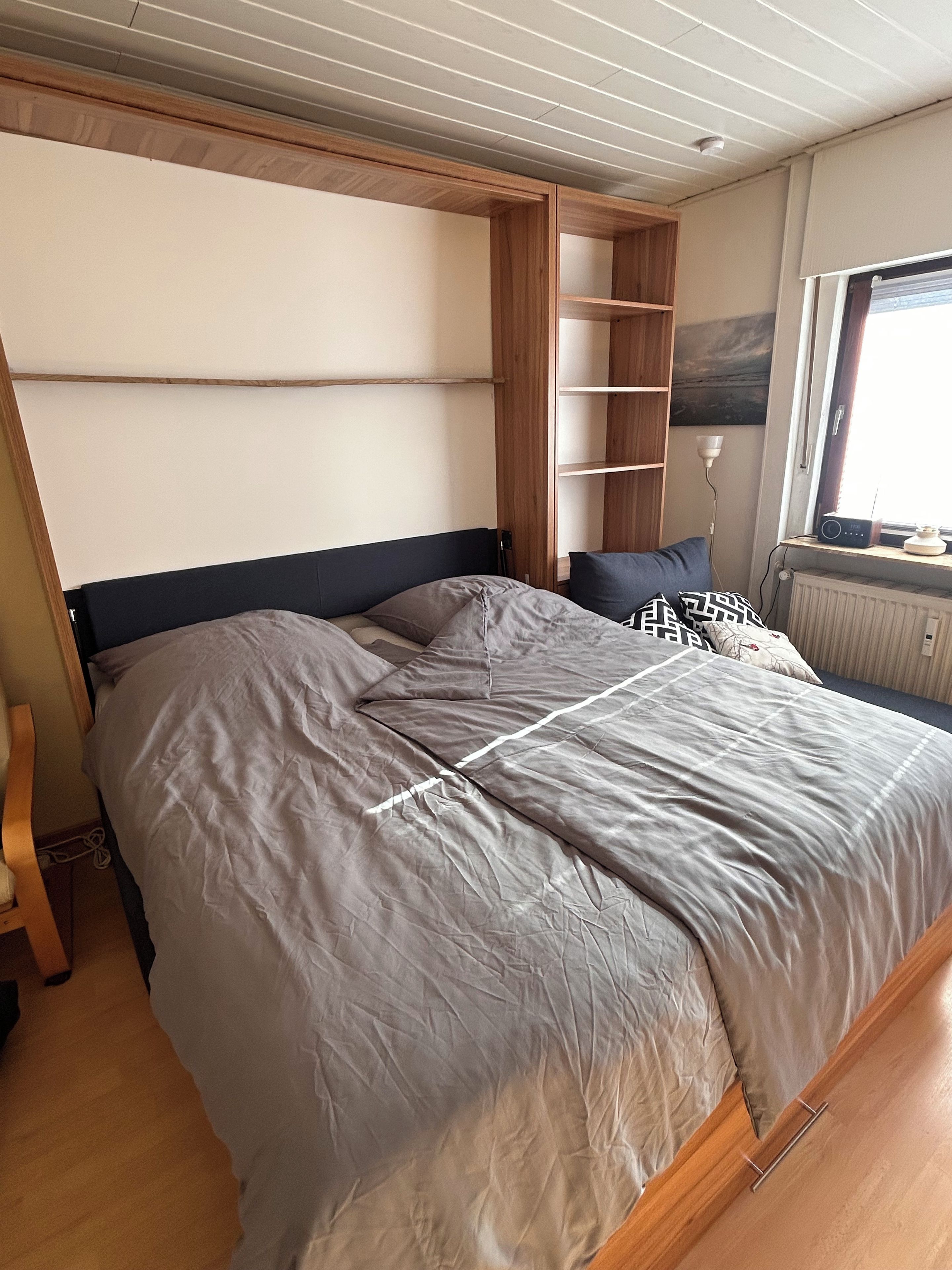 Camera da letto con un letto, una testiera in legno, una scaffalatura e una finestra vista.