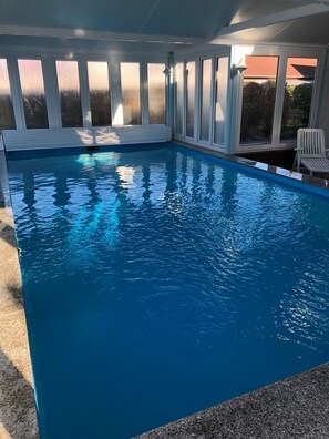 An indoor swimming pool with clear blue water, surrounded by large windows and a white chair. - A cozy retreat for a getaway by the sea; dogs welcome—with a pool and sauna (Butjadingen)