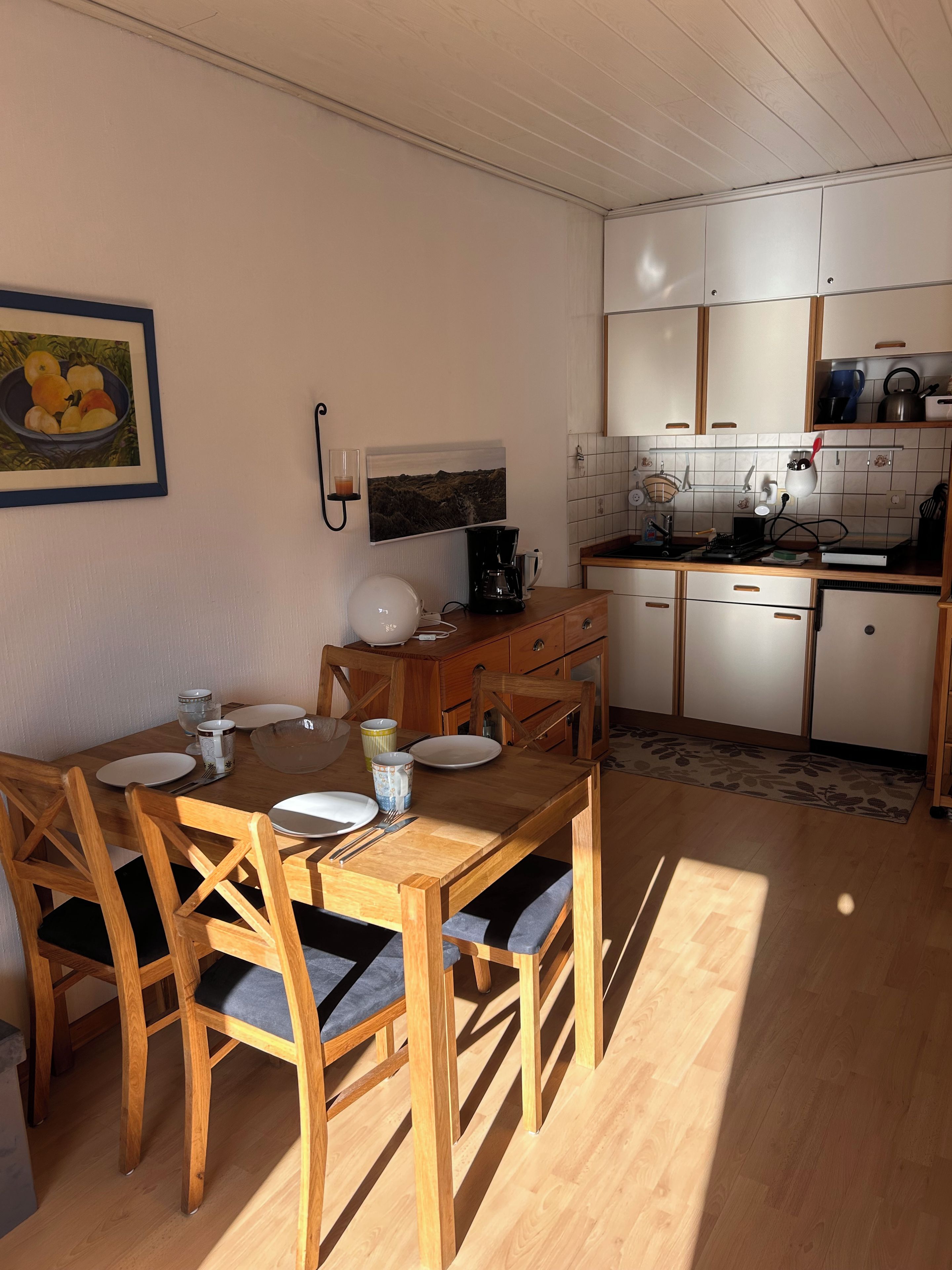 Une cuisine compacte avec des meubles en bois, une table à manger avec des chaises et une machine à café.