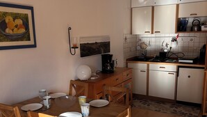 A compact kitchen with wooden cabinets, a dining table with chairs, and a coffee maker.