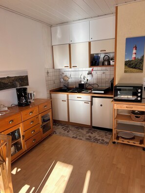 A compact kitchen with white cabinets, a wooden countertop, a coffee maker, a kettle, and a toaster.