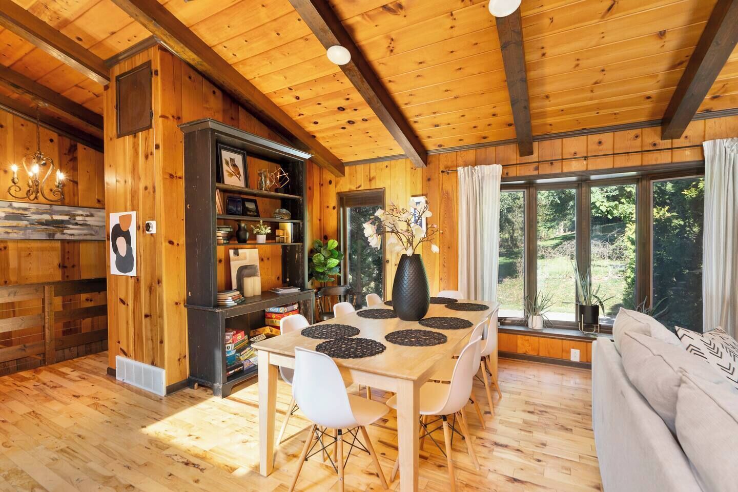 Un interno in legno con un tavolo da pranzo, sedie, un divano e un'ampia finestra.